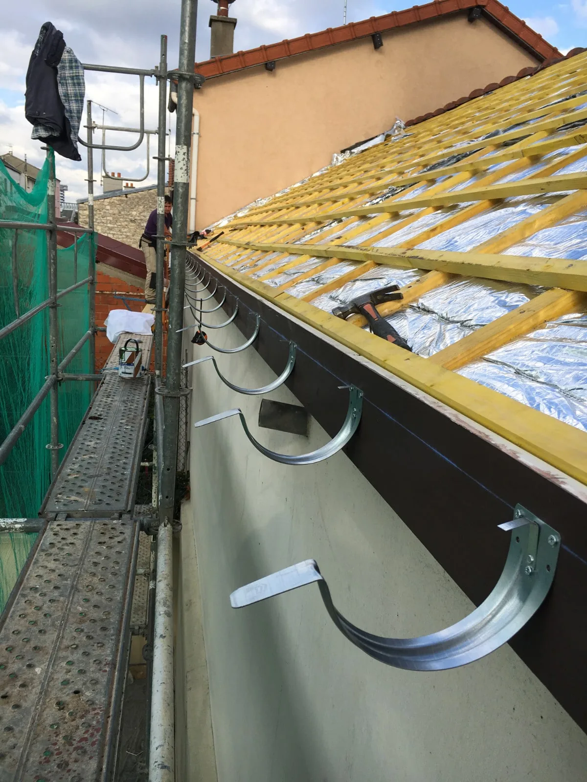 Gouttière posée en rive de toit pendant une rénovation de toiture, chevrons et liteaux neufs